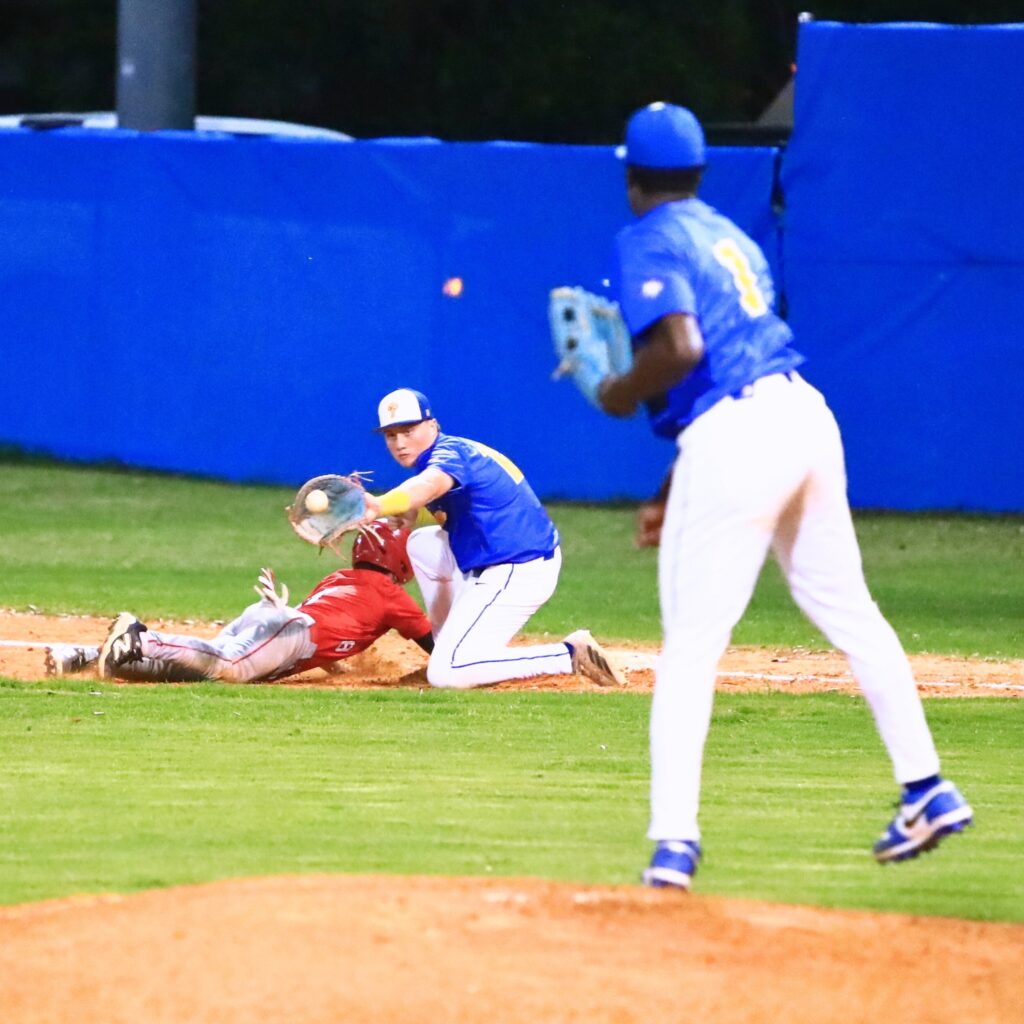 Santa Fe's Dylan Doria (8) dives back to first base ahead of a pickoff throw to Newberry's Brantley McCoy (12). Photo by C.J. Gish