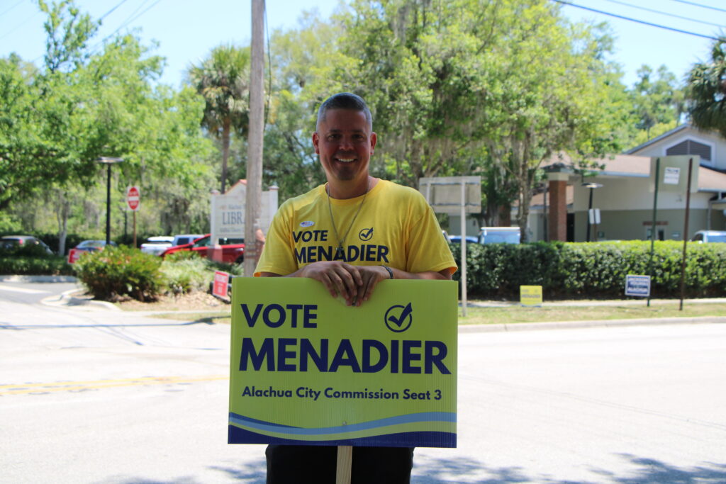Bill Menadier waved signs outside the Alachua Library on Tuesday.
