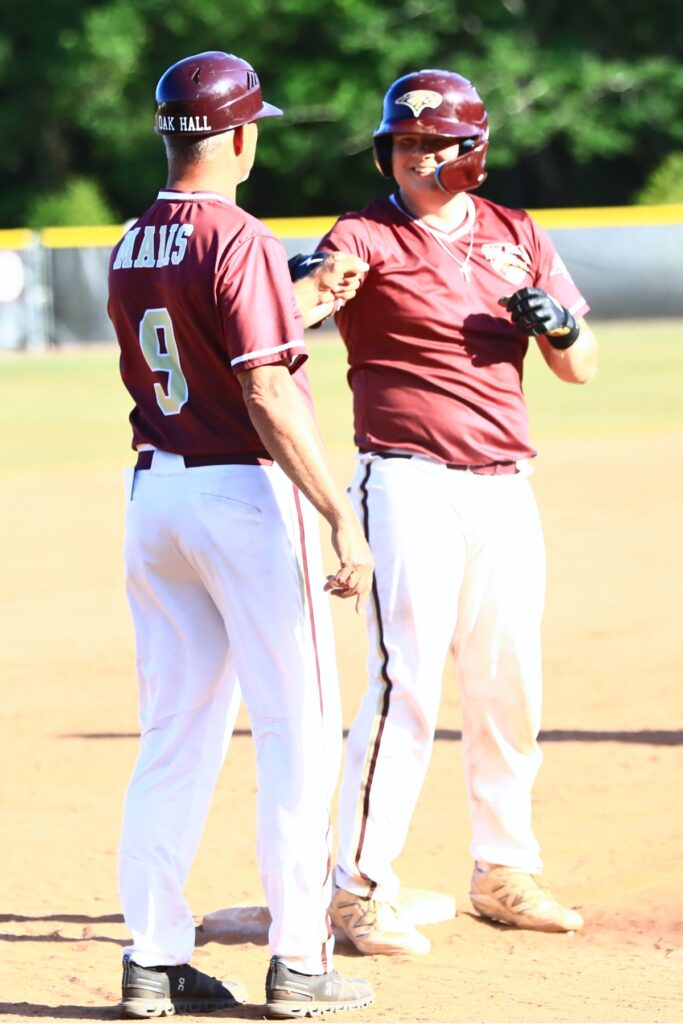 Oak Hall's Cameron Currier first bumps coach Kevin Maris after driving in three runs and advancing to third base in the fourth inning against Countryside Christian. Photo by C.J. Gish