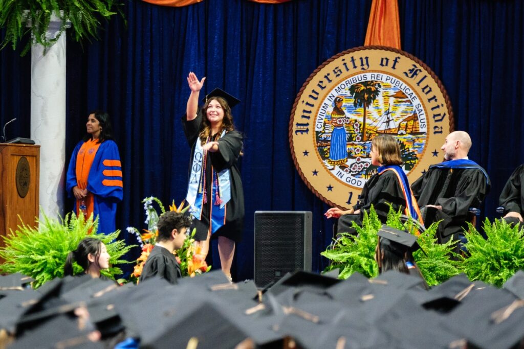 A student does the Gator Chomp while walking across the stage