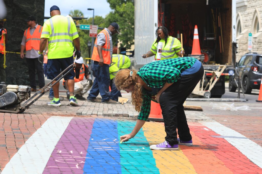 Deborah Hart uses chalk to protest the removal of Gainesville's rainbow crosswalk happening behind her. Photo by Seth Johnson