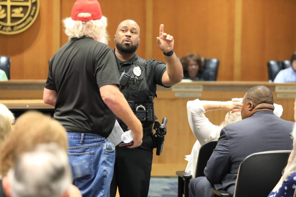 At the request of Mayor Walter Welch, a police officer escorts a resident out of the meeting for clapping. Photo by Lillian Hamman