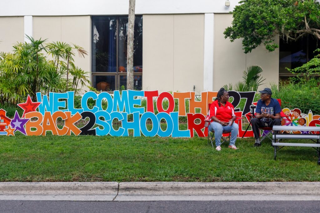 Volunteers sit beside a Welcome to the 27th Back to School sign before the 27th annual Back to School event at Santa Fe College on Saturday. The event provided local students with free school supplies, haircuts and other community resources ahead of the new school year.