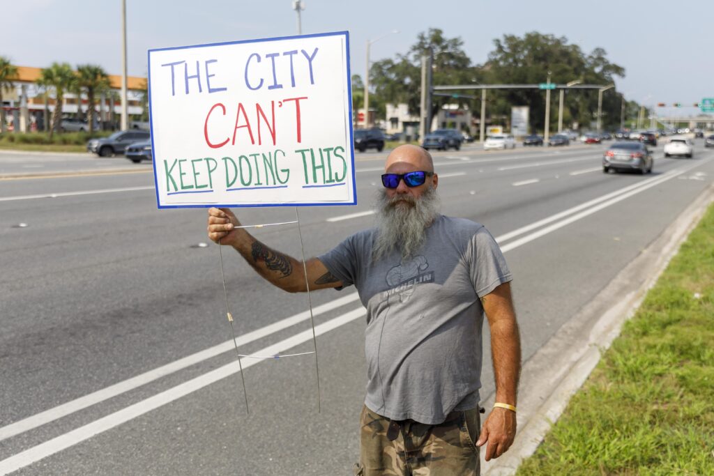 Paul Cellon holds a sign reading Tree City USA!! during a protest along Archer Road in Gainesville, Fla., on Wednesday, July 29, 2026. Cellon joined other Riceland residents protesting the clear-cutting of hundreds of trees for construction of Gainesville Fire Station #9