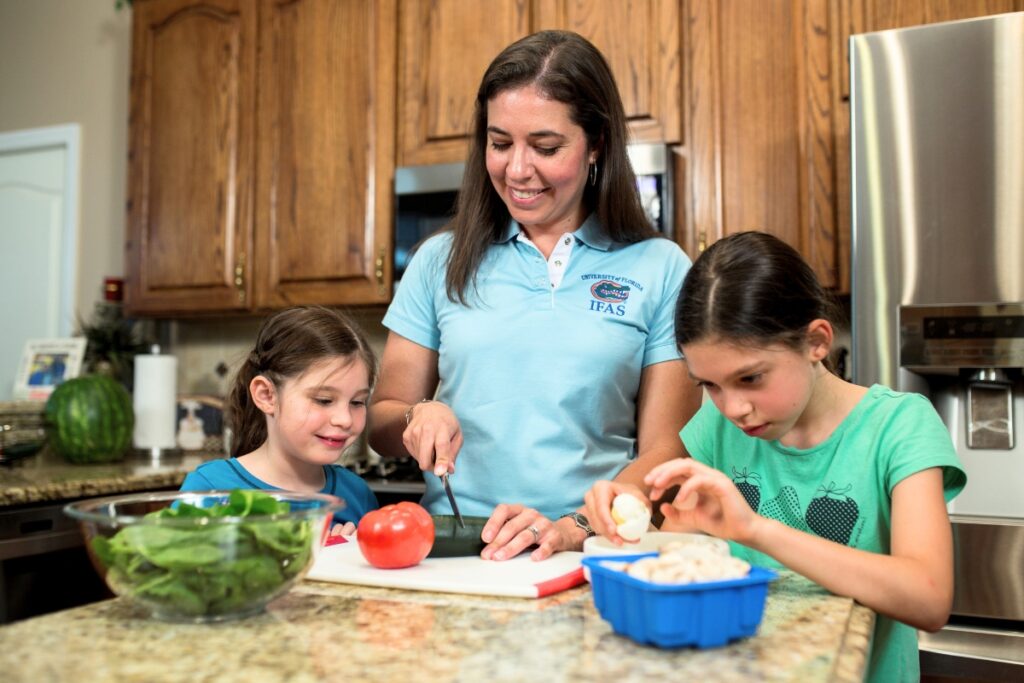 Karla Shelnutt, UFIFAS professor and associate dean of UFIFAS Extension Engagement cutting vegetables with her daughters in a kitchen practicing meal prep. Photo by Tyler Jones - UF-IFAS