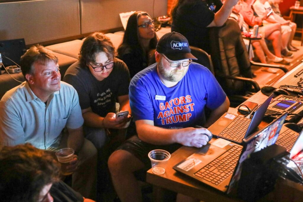 Tyler Forest (hat), chair of the Alachua County Democratic Party, tracks election results at Heartwood Soundstage on Tuesday. Photo by Walker Smith
